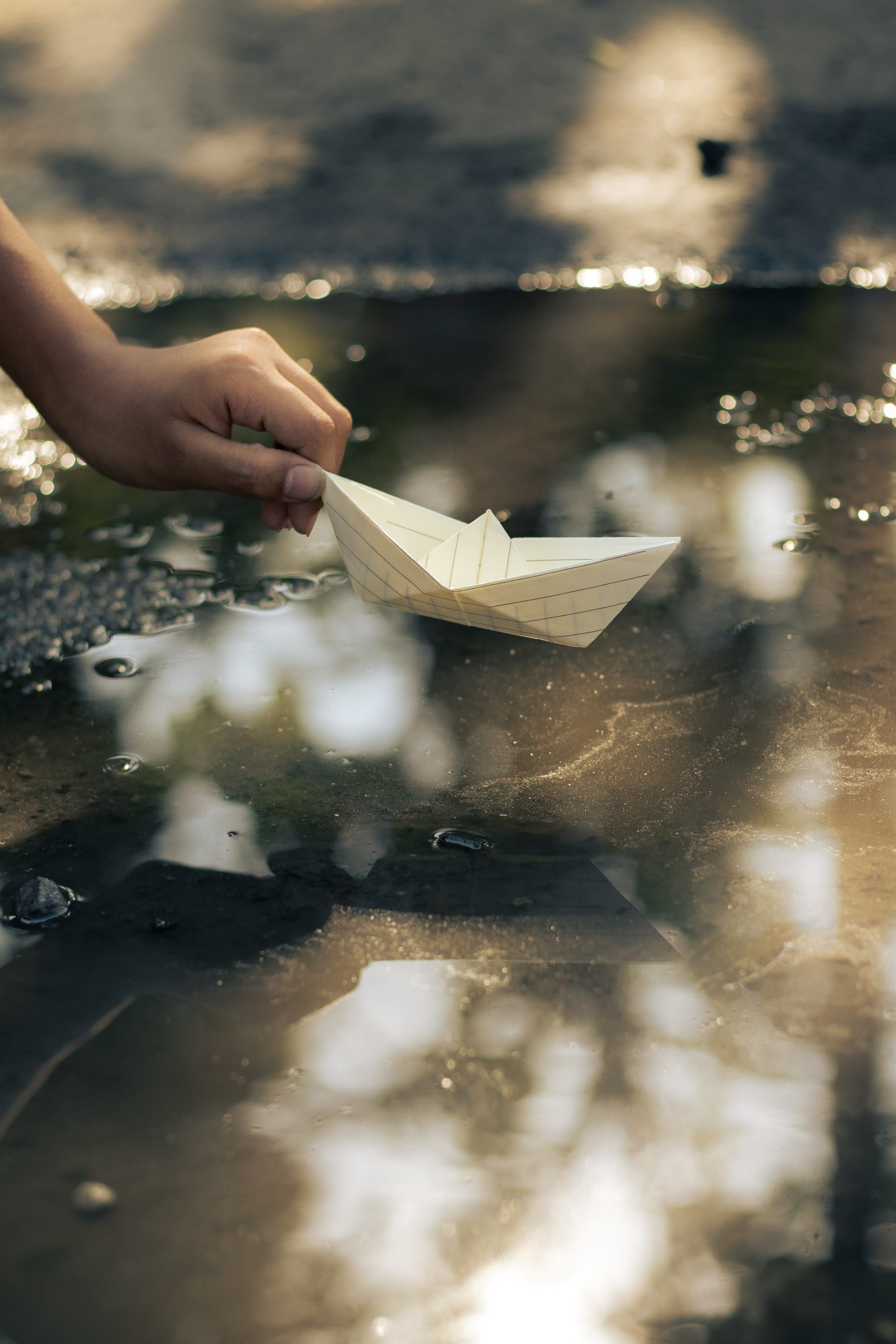 A hand placing a paper boat into a puddle