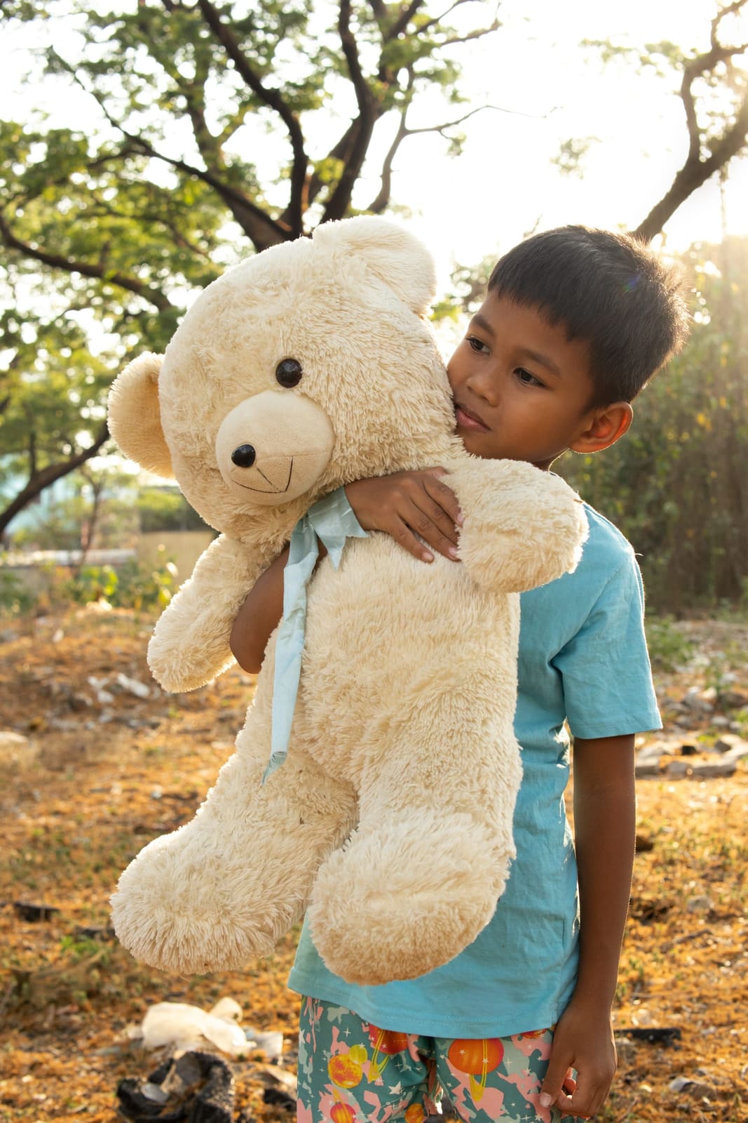 A boy holding a teddy bear under golden trees